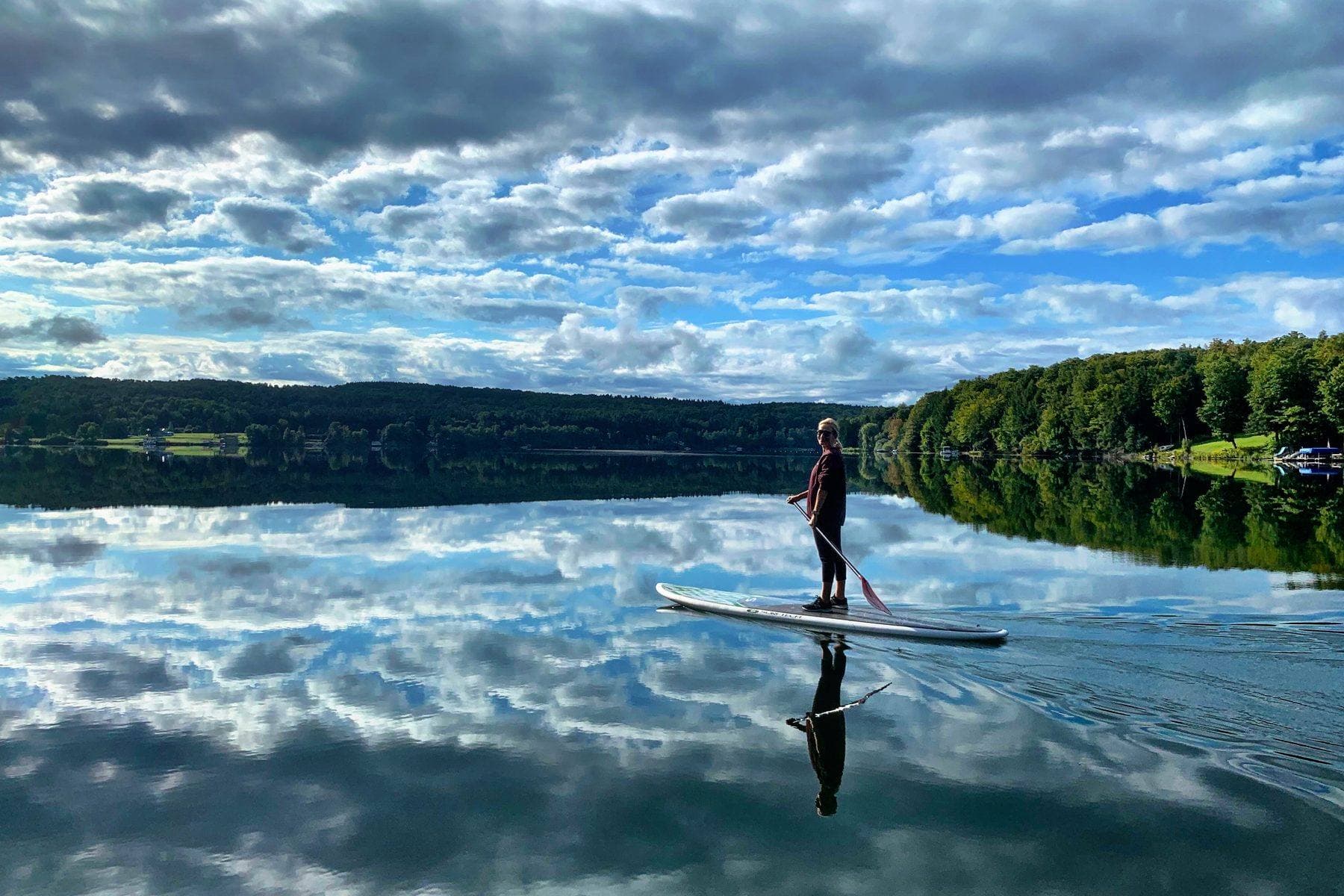 Paddleboarding on a still lake under broken cloud.